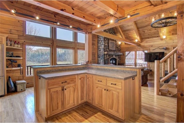 kitchen with light wood-type flooring, wood ceiling, wooden walls, beam ceiling, and a stone fireplace