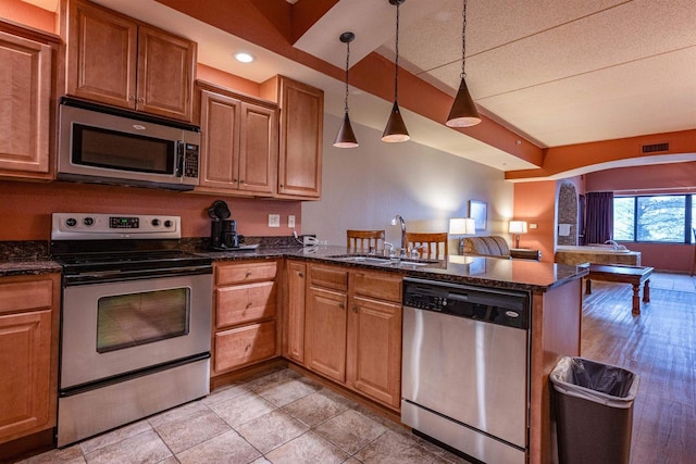 kitchen with dark stone counters, sink, appliances with stainless steel finishes, decorative light fixtures, and kitchen peninsula