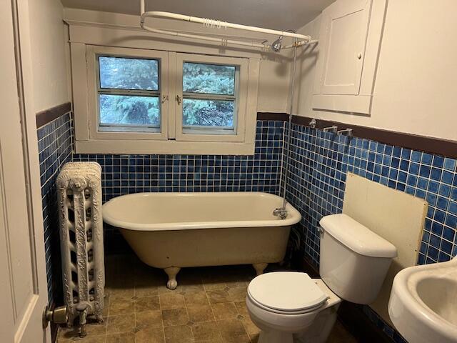 bathroom with toilet, sink, tile walls, and a washtub