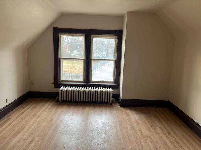 additional living space featuring radiator heating unit, light hardwood / wood-style floors, and vaulted ceiling