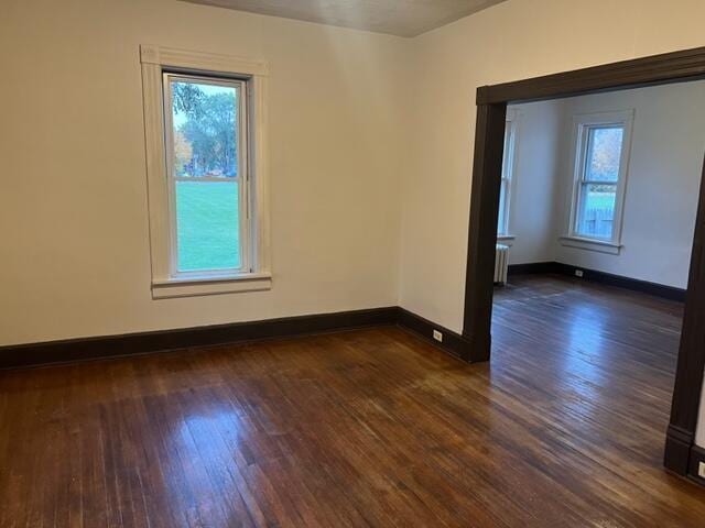 unfurnished room with dark hardwood / wood-style flooring, radiator, and a wealth of natural light