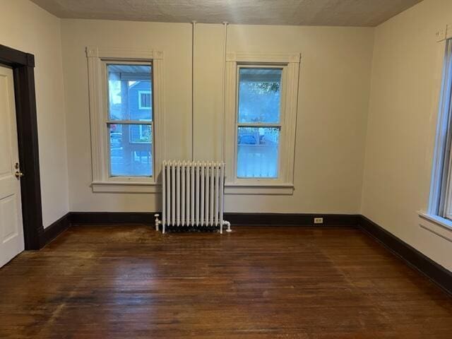 spare room featuring radiator heating unit and dark hardwood / wood-style flooring