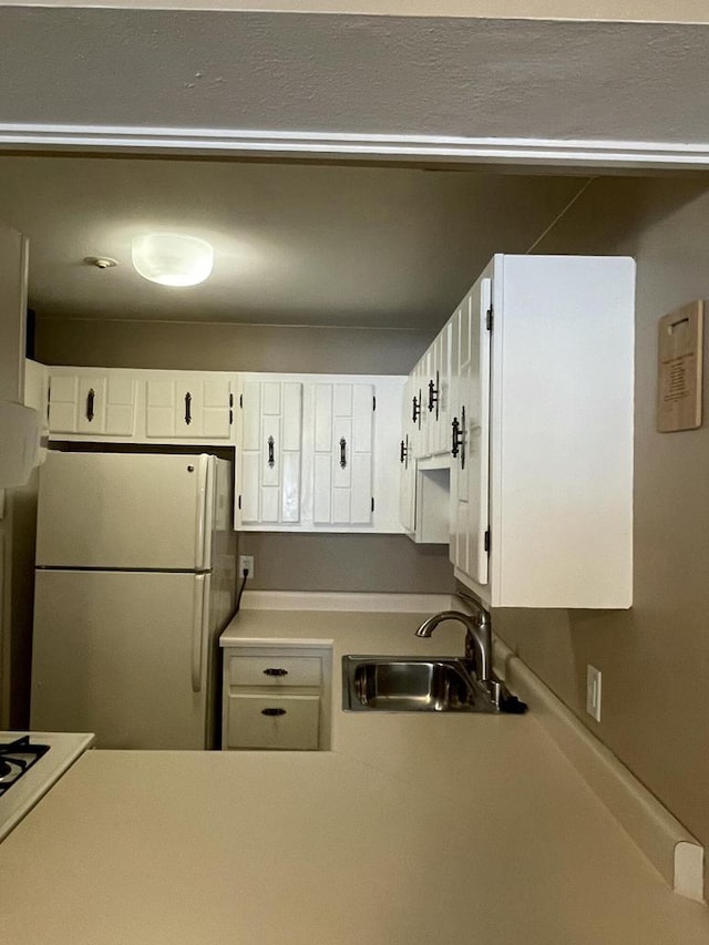 kitchen featuring white fridge, cooktop, white cabinetry, and sink