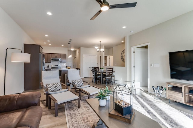 living room with ceiling fan with notable chandelier and light wood-type flooring