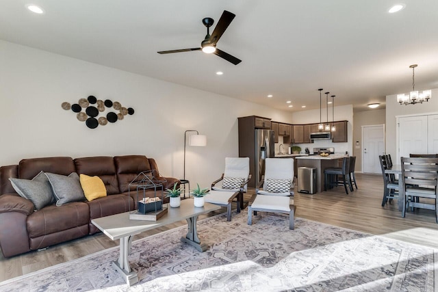 living room featuring ceiling fan with notable chandelier, light wood-type flooring, and sink