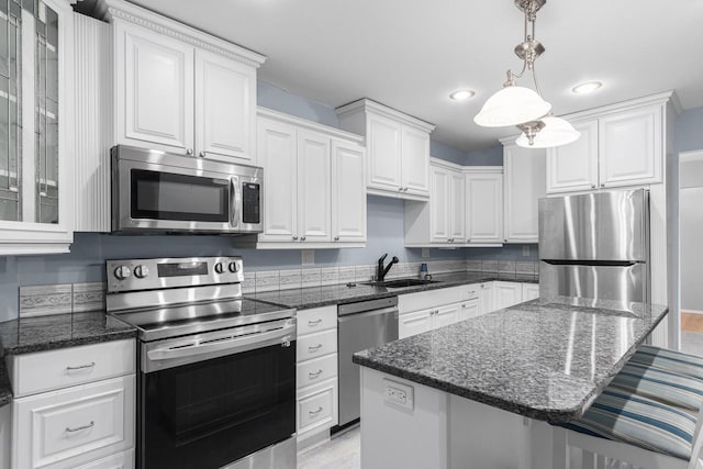 kitchen featuring a kitchen bar, white cabinetry, stainless steel appliances, and decorative light fixtures