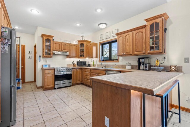 6461 Blue Heron Pointe Dr, Waterford, WI 53185 - kitchen with kitchen peninsula, appliances with stainless steel finishes, a kitchen bar, tile counters, and light tile patterned flooring