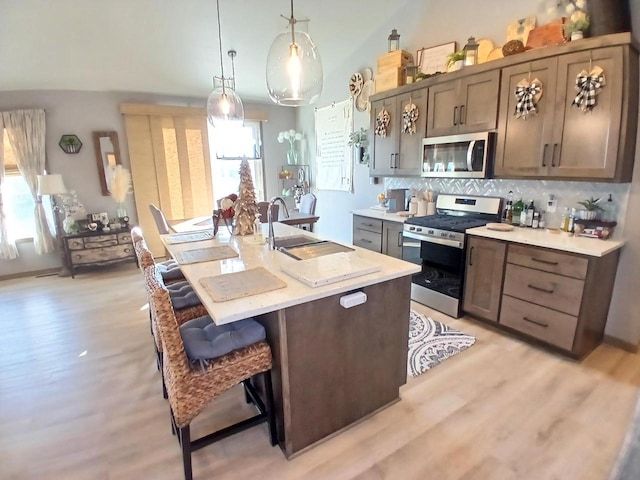 kitchen featuring decorative backsplash, appliances with stainless steel finishes, a kitchen island with sink, pendant lighting, and a breakfast bar area