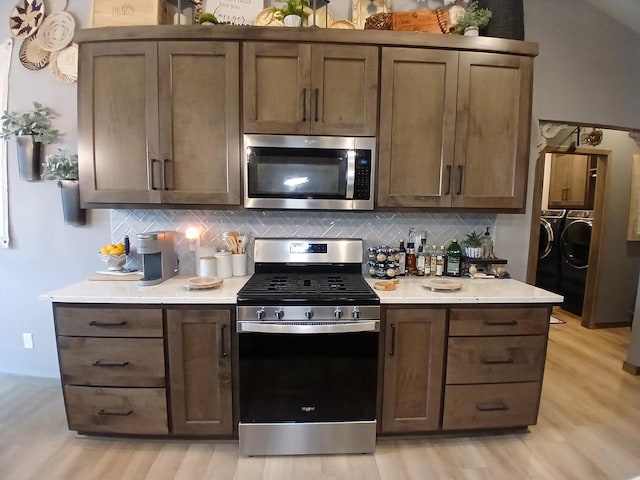 kitchen with washer and clothes dryer, light hardwood / wood-style floors, stainless steel appliances, and tasteful backsplash