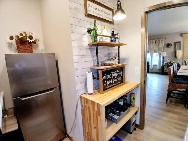 kitchen with stainless steel refrigerator, wooden walls, pendant lighting, and hardwood / wood-style flooring