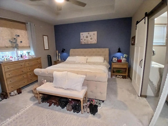 bedroom with ceiling fan, a barn door, a raised ceiling, and light carpet