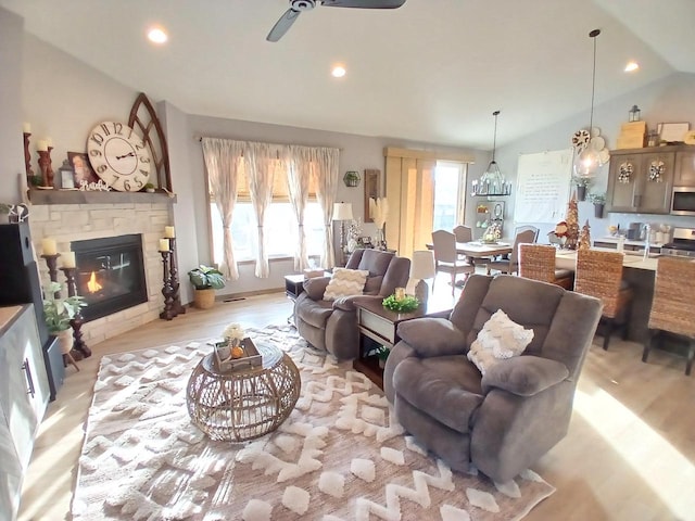 living room featuring a stone fireplace, a wealth of natural light, ceiling fan, and lofted ceiling