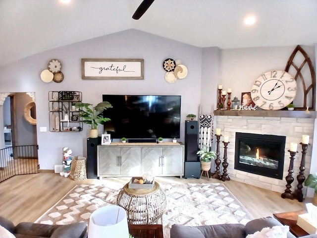 living room featuring a stone fireplace, light hardwood / wood-style flooring, and vaulted ceiling