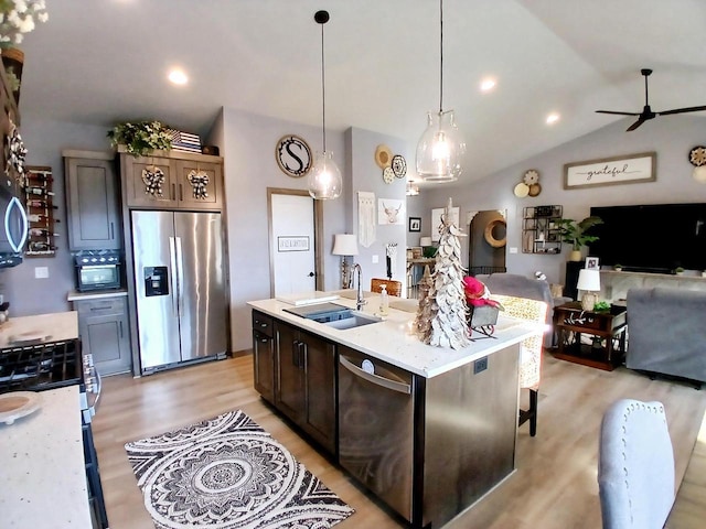 kitchen with pendant lighting, lofted ceiling, a kitchen island with sink, sink, and appliances with stainless steel finishes