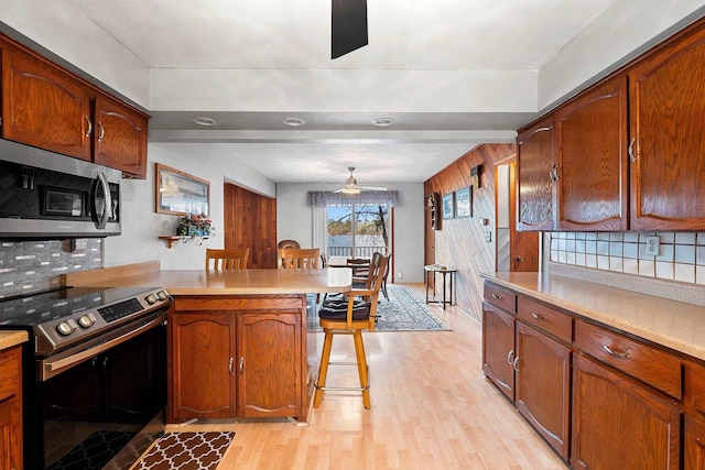 kitchen featuring a kitchen breakfast bar, electric range, ceiling fan, tasteful backsplash, and kitchen peninsula