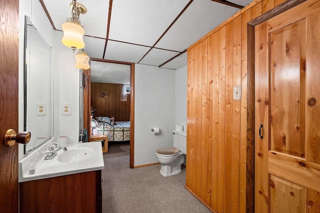 bathroom featuring a paneled ceiling, wooden walls, vanity, and toilet