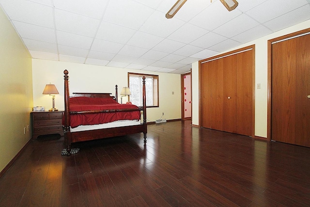 bedroom with multiple closets, a drop ceiling, dark wood-type flooring, and ceiling fan