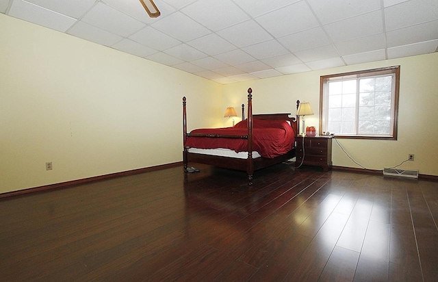 bedroom with ceiling fan, a drop ceiling, and wood-type flooring