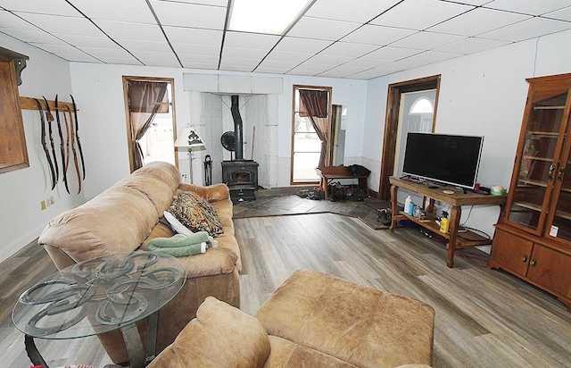 living room with wood-type flooring, a wood stove, and a drop ceiling