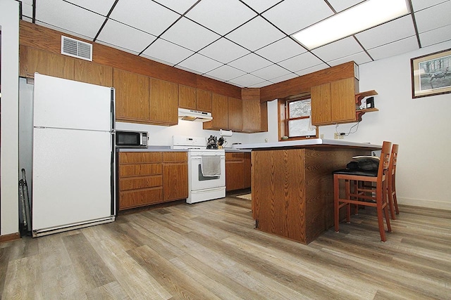 kitchen with a paneled ceiling, white appliances, light wood-type flooring, kitchen peninsula, and a breakfast bar area