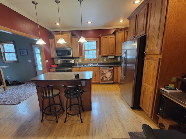 kitchen featuring appliances with stainless steel finishes, sink, a center island, light hardwood / wood-style floors, and hanging light fixtures