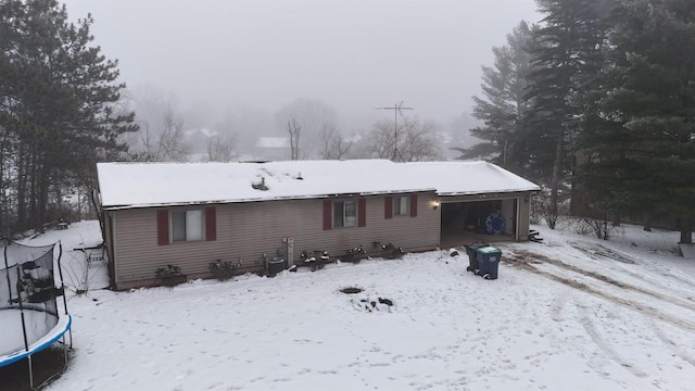 snow covered rear of property featuring a garage and a trampoline