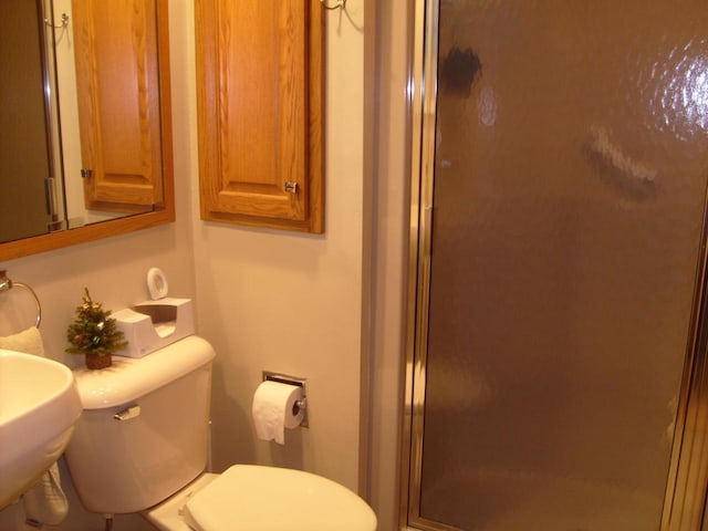 bathroom featuring toilet, a shower with door, and sink