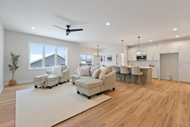 living room featuring ceiling fan with notable chandelier and light hardwood / wood-style flooring