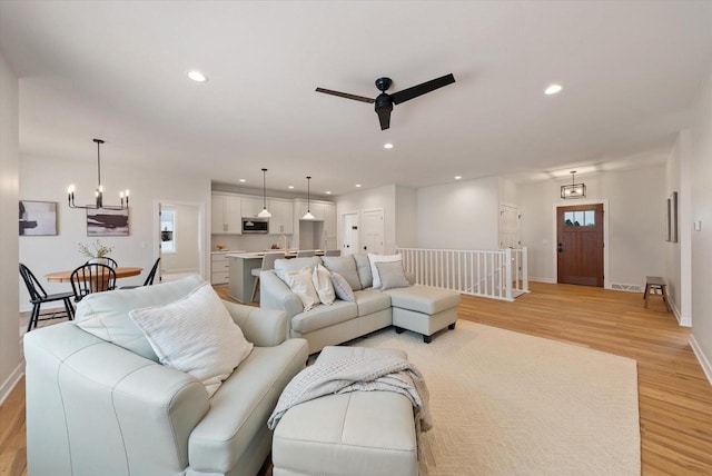 living room featuring ceiling fan with notable chandelier and light hardwood / wood-style flooring