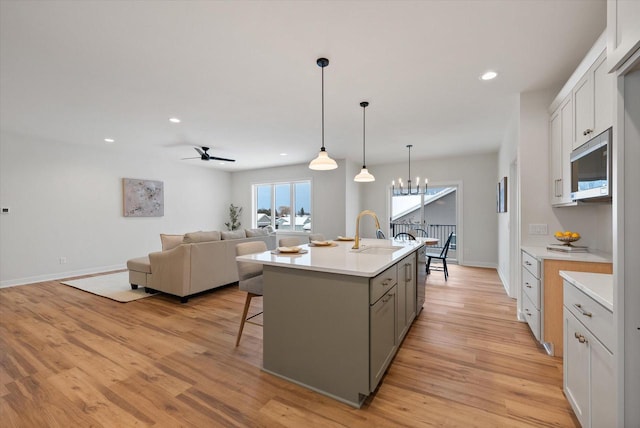 kitchen featuring white cabinetry, sink, pendant lighting, a kitchen island with sink, and ceiling fan with notable chandelier