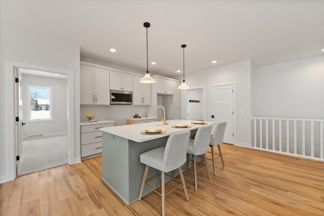 kitchen featuring a kitchen breakfast bar, light wood-type flooring, a kitchen island with sink, white cabinetry, and hanging light fixtures