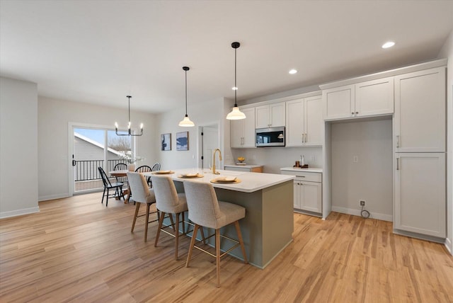 kitchen with pendant lighting, light hardwood / wood-style floors, white cabinetry, and an island with sink