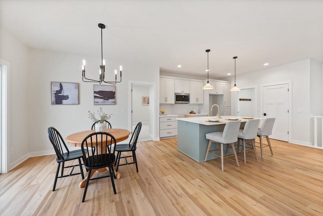 kitchen featuring light hardwood / wood-style flooring, an island with sink, decorative light fixtures, a kitchen bar, and white cabinets