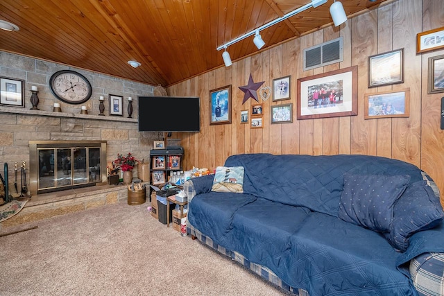 carpeted living room featuring wood ceiling, wooden walls, a stone fireplace, and track lighting