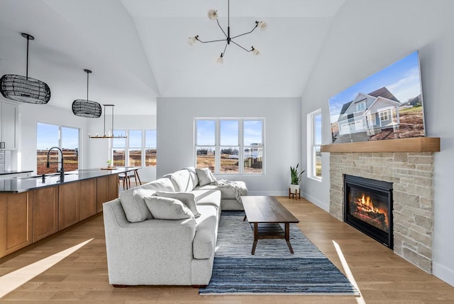 living room with a chandelier, light wood-type flooring, high vaulted ceiling, and a stone fireplace