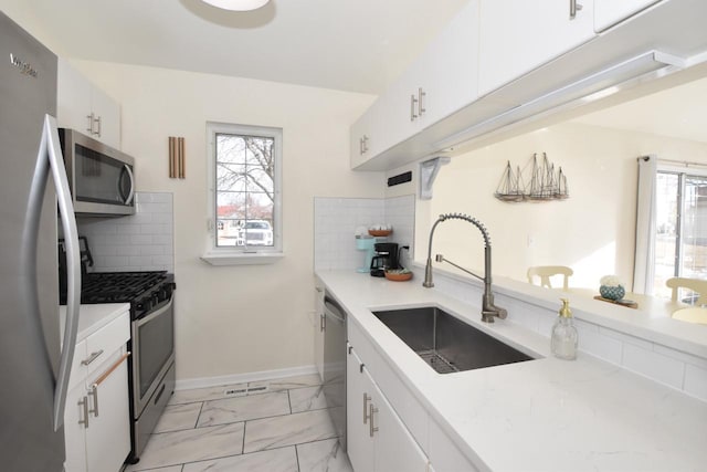 kitchen featuring sink, stainless steel appliances, a healthy amount of sunlight, white cabinets, and decorative backsplash