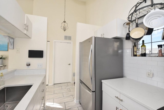 kitchen with decorative light fixtures, white cabinetry, sink, stainless steel fridge, and backsplash