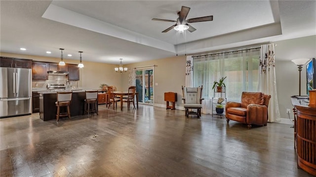 living room with dark hardwood / wood-style floors, a raised ceiling, and ceiling fan with notable chandelier