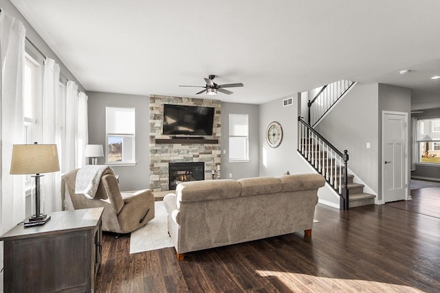 living room featuring a stone fireplace, ceiling fan, dark hardwood / wood-style flooring, and a healthy amount of sunlight