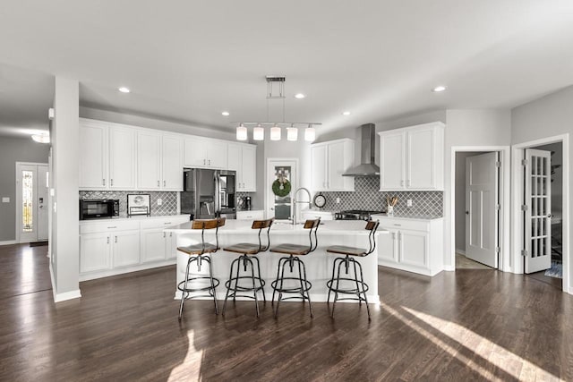 kitchen featuring stainless steel fridge with ice dispenser, white cabinetry, a kitchen island with sink, and wall chimney exhaust hood