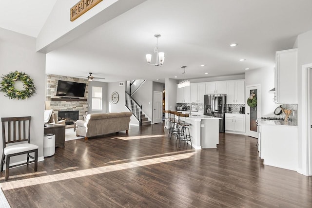 living room featuring dark hardwood / wood-style flooring, ceiling fan with notable chandelier, vaulted ceiling, sink, and a stone fireplace