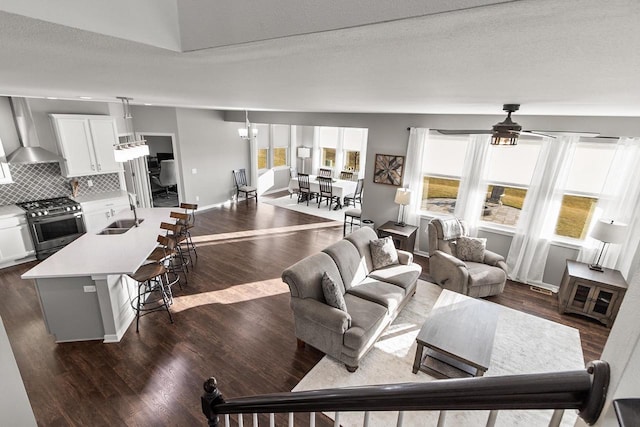 living room with a textured ceiling, ceiling fan with notable chandelier, dark hardwood / wood-style flooring, and sink