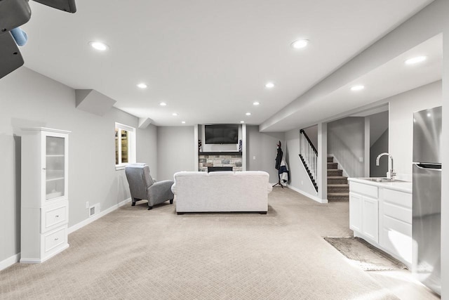 carpeted living room featuring a stone fireplace and sink