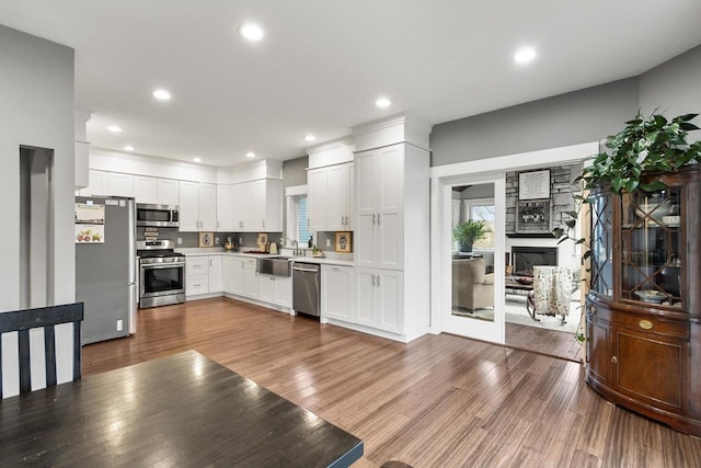 kitchen featuring appliances with stainless steel finishes, sink, hardwood / wood-style flooring, white cabinetry, and a stone fireplace