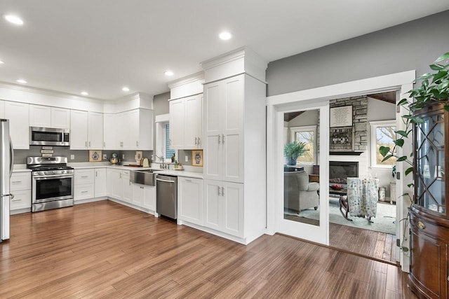 kitchen with sink, a fireplace, light hardwood / wood-style floors, white cabinetry, and stainless steel appliances