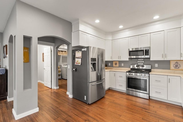 kitchen with appliances with stainless steel finishes, hardwood / wood-style flooring, white cabinetry, and washer / dryer