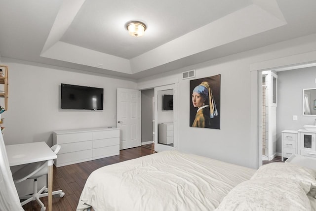 bedroom featuring dark hardwood / wood-style flooring, connected bathroom, and a raised ceiling