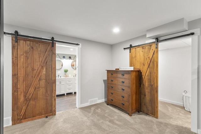 unfurnished bedroom with light carpet, a barn door, ensuite bath, and sink