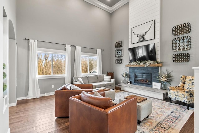 living room featuring crown molding, a towering ceiling, a fireplace, and dark wood-type flooring