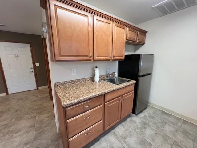 kitchen with black fridge, light stone countertops, and sink